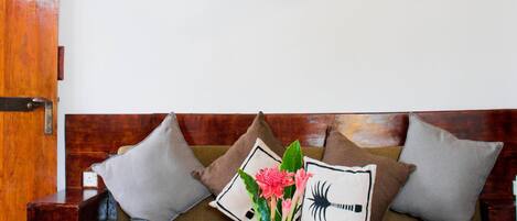 A wooden sofa with cushions, a coffee table with a book, and a vase with flowers.