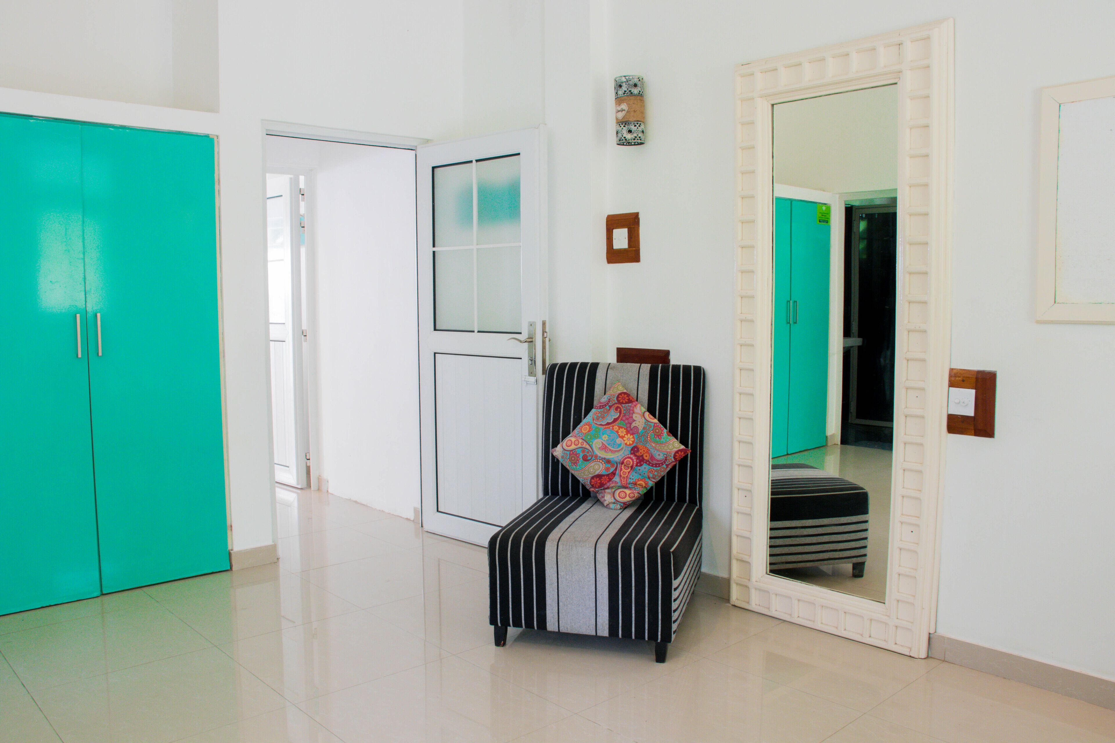 A room with a teal wardrobe, a striped chair with a patterned cushion, and a mirror with a decorative frame.