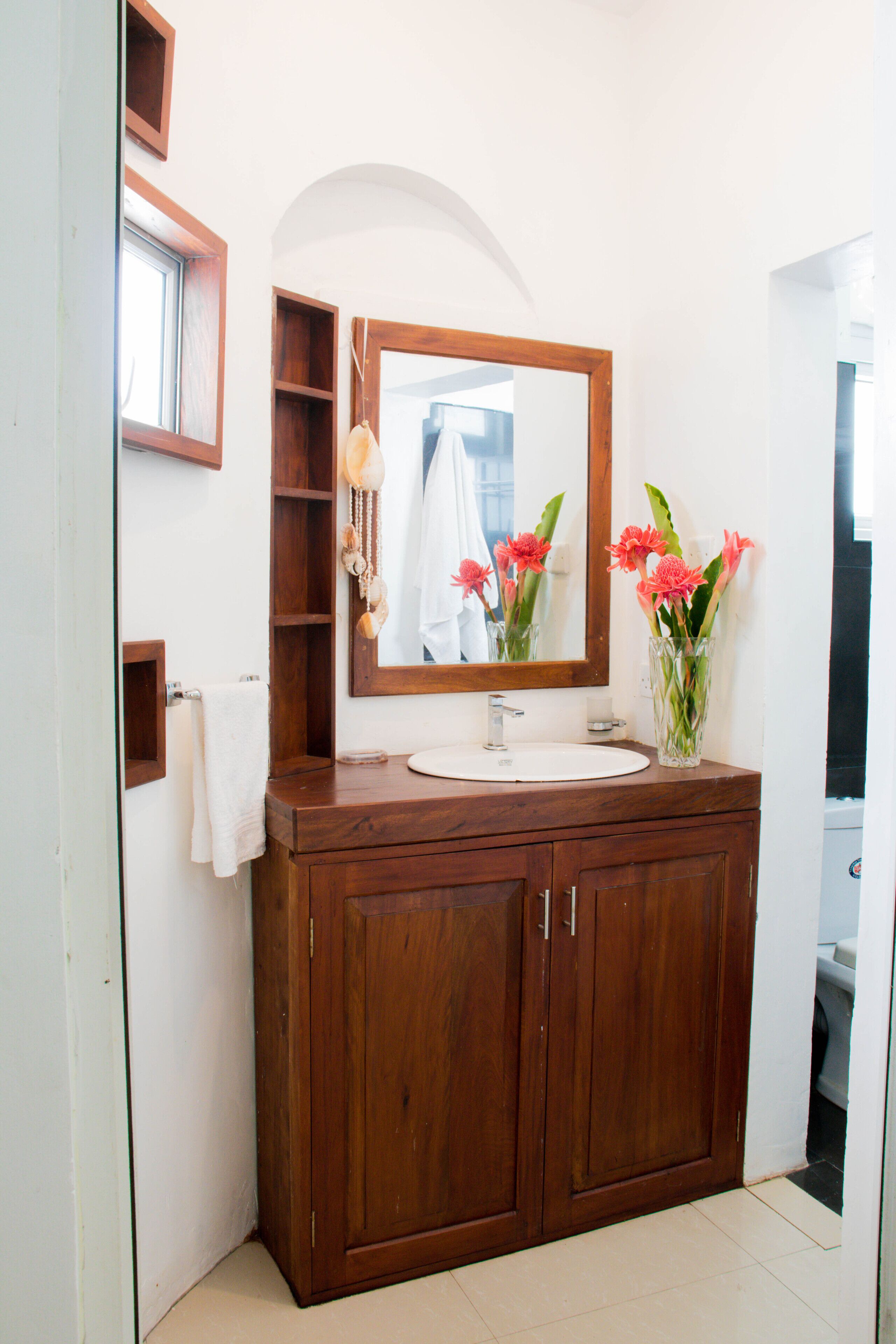 Une salle de bain avec un meuble-lavabo en bois, un miroir, un évier et un vase rempli de fleurs.