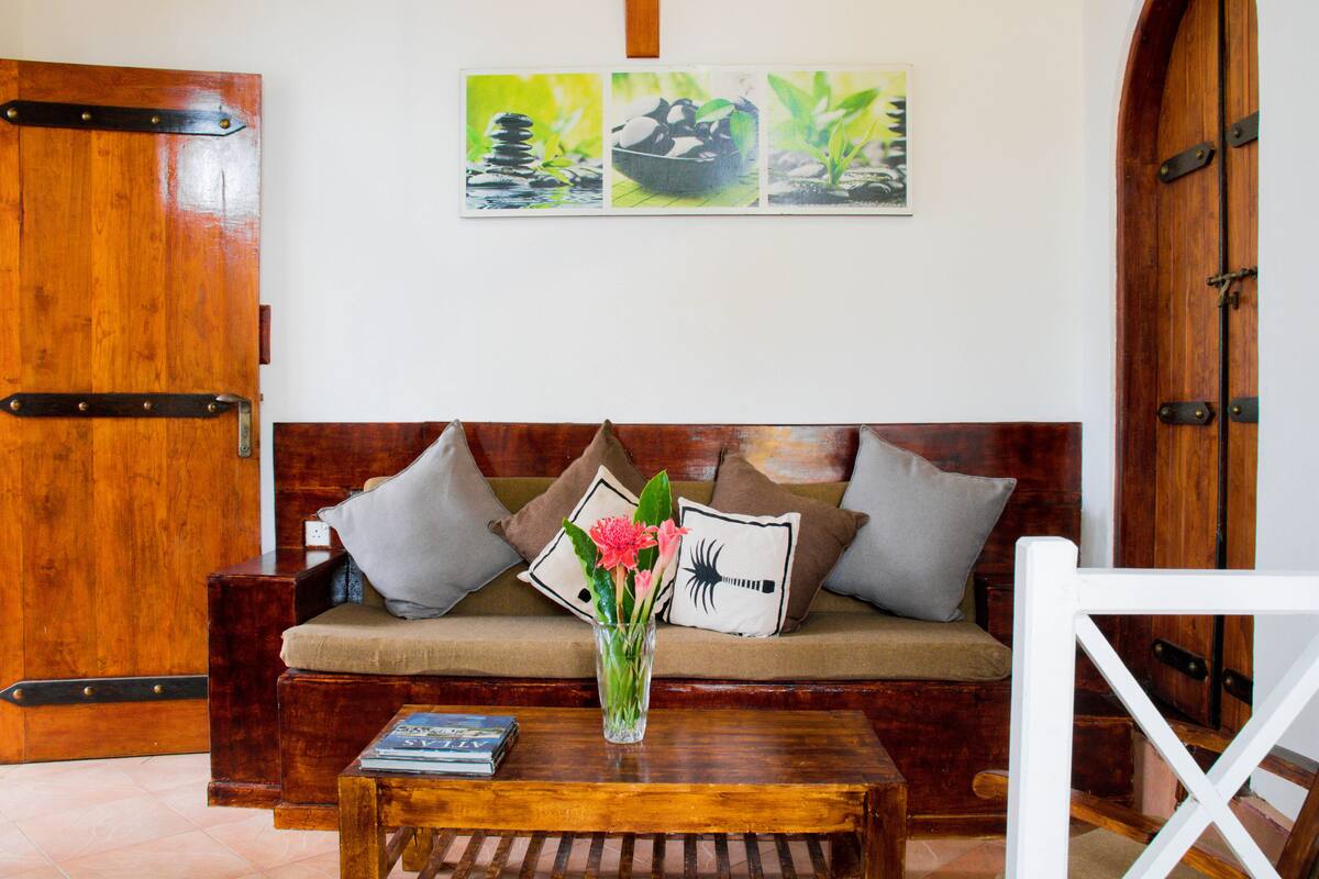 A wooden door, a wooden bench, a wooden table, a sofa with cushions, and a wall with a framed picture.