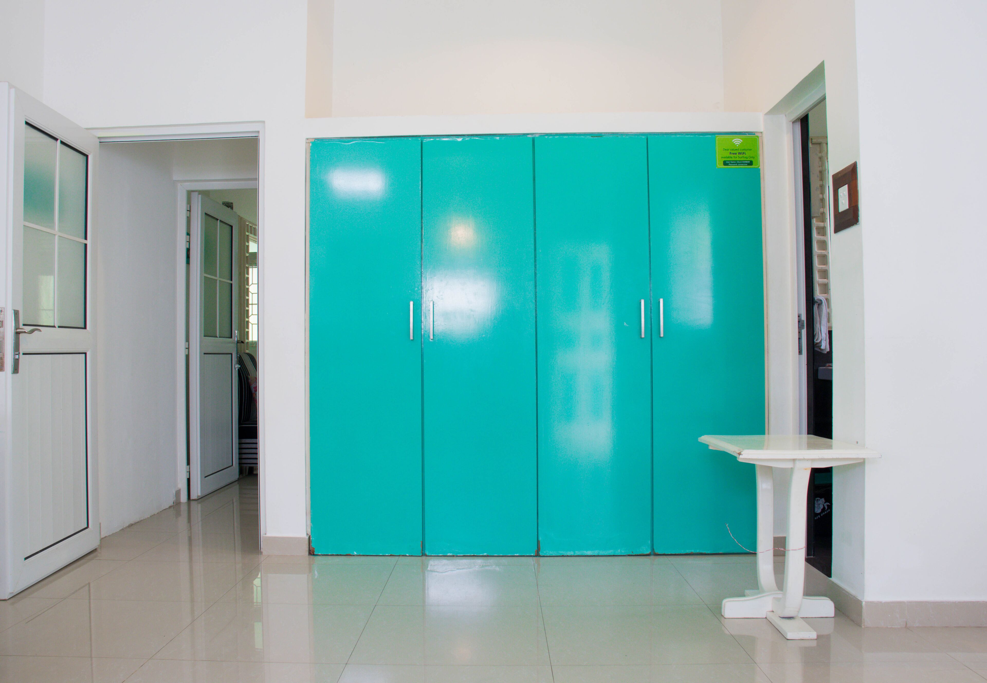 Un pasillo con armarios color turquesa, una mesa blanca y una puerta que da a otra habitación.