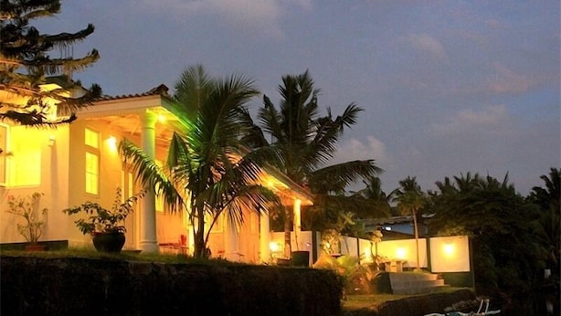 Casa ben il·luminada amb una font al davant, envoltada de palmeres i un cel serè.