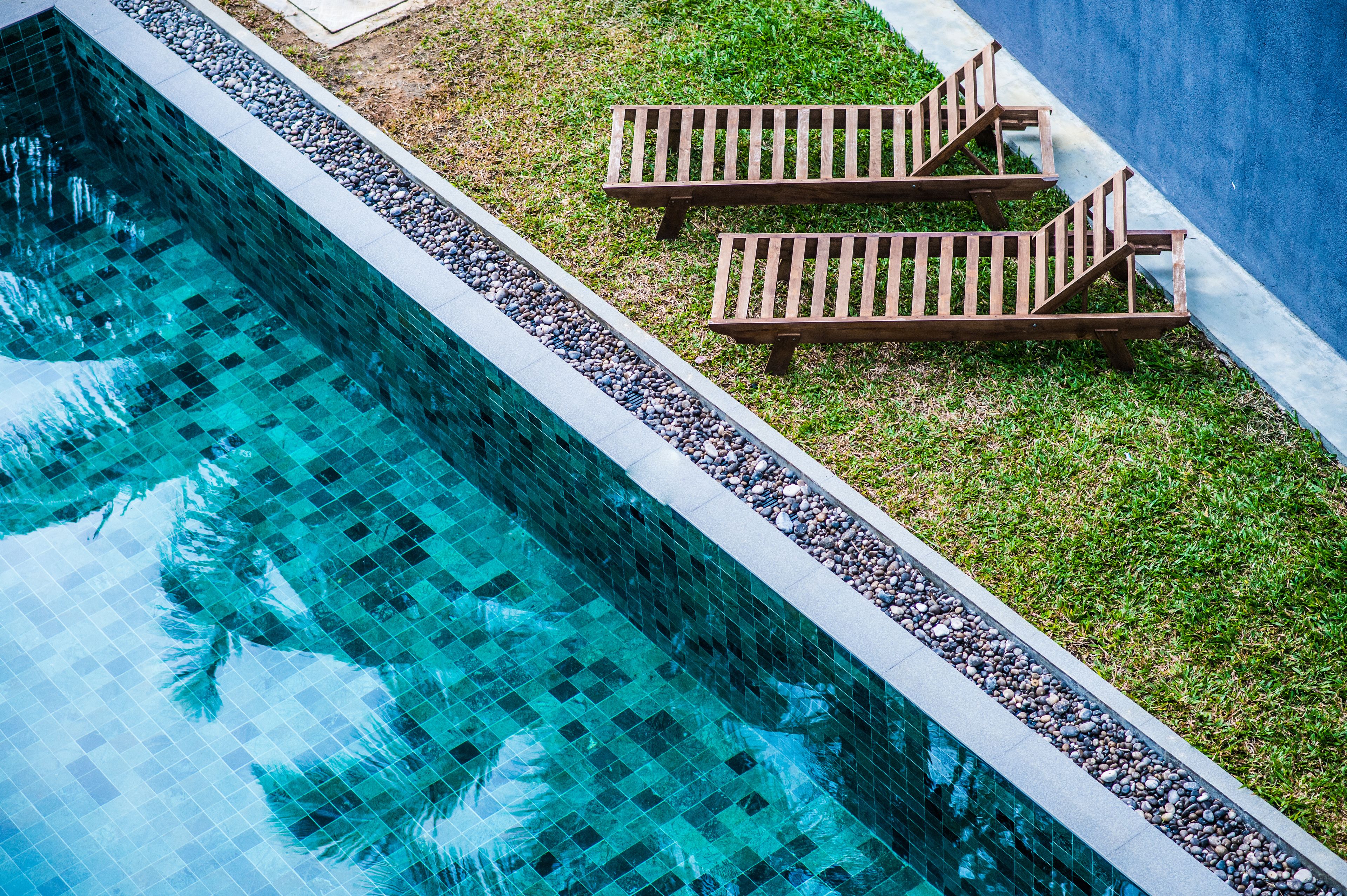 A swimming pool with a tiled edge and two wooden loungers on a grassy area.