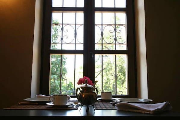 A table with a teapot and cups by a window with a view of greenery.