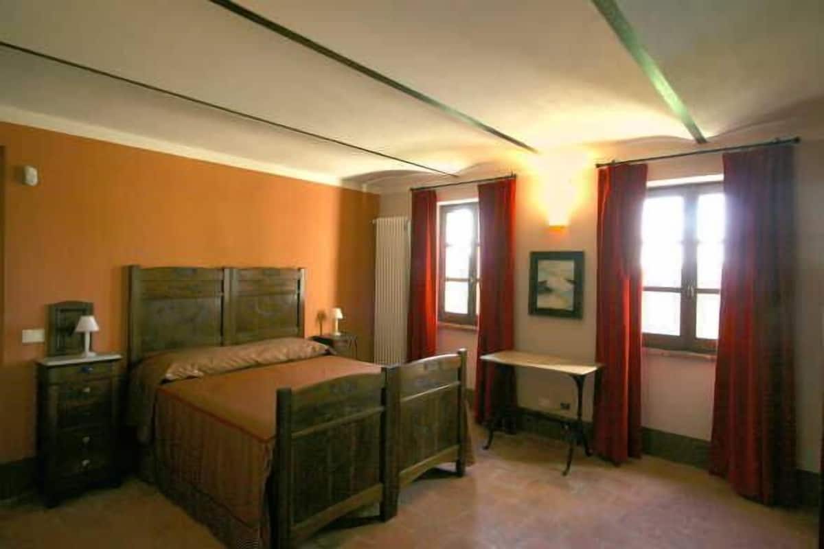 A bedroom with a wooden bed, a bedside table, a dresser, and a window with red curtains.