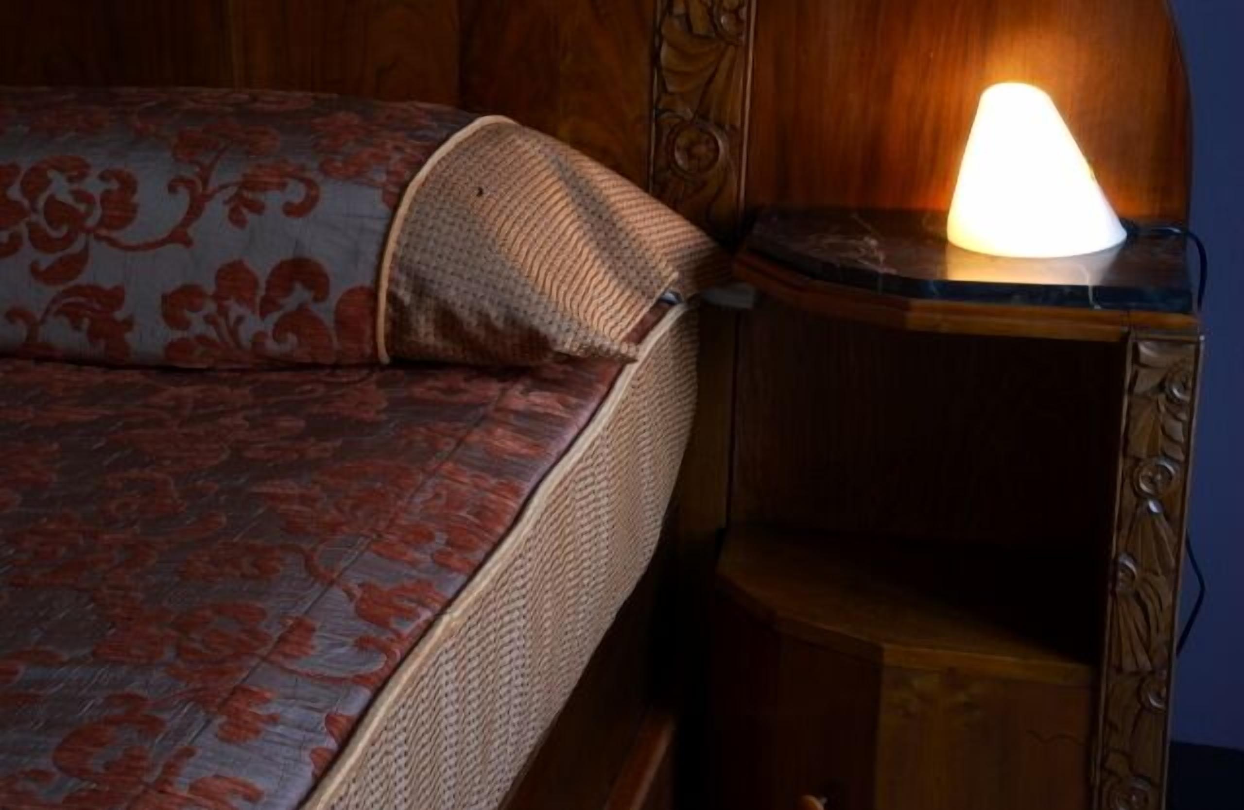 A bed with a patterned bedspread and a bedside lamp on a wooden nightstand.