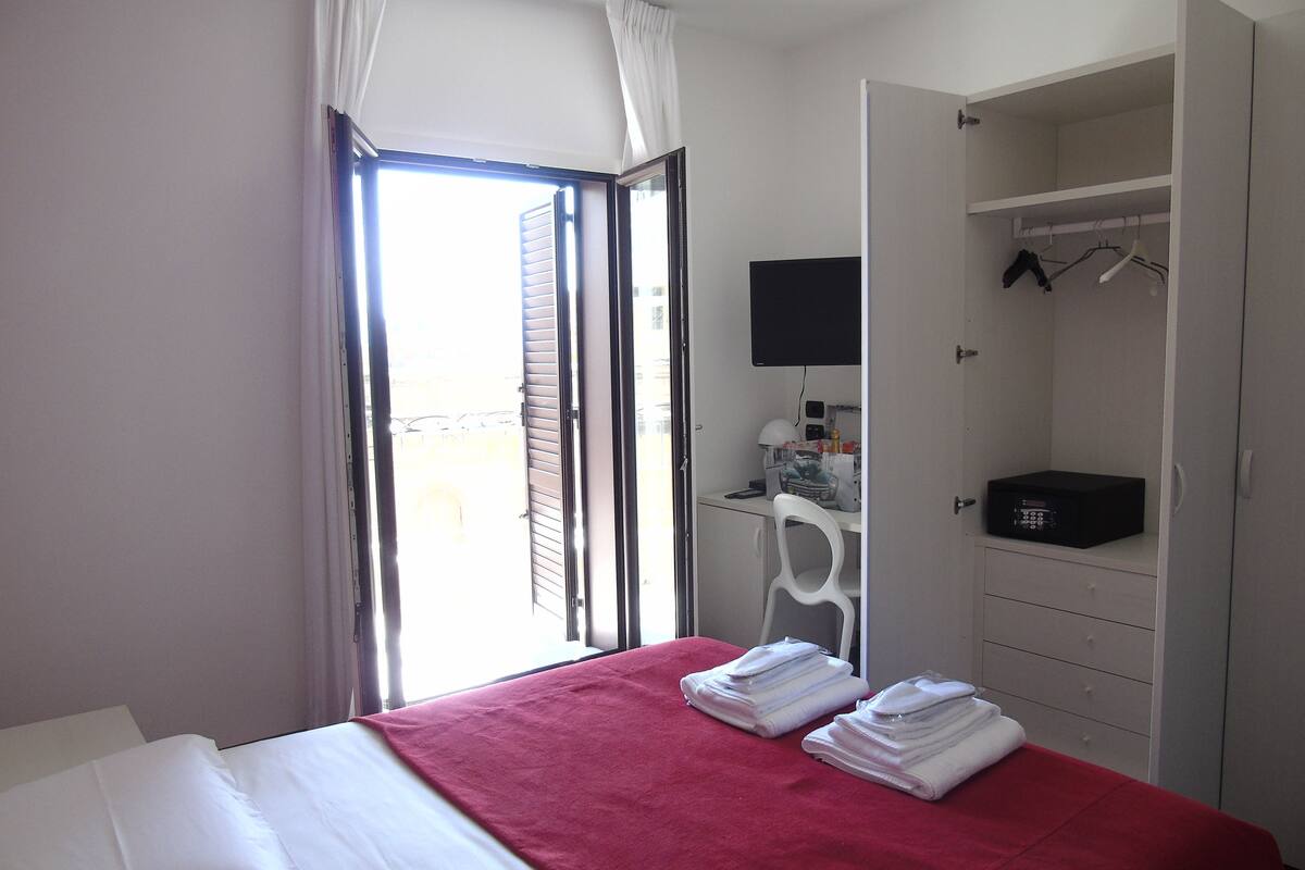 A hotel room with a bed, a desk, a chair, a wardrobe, and a television.