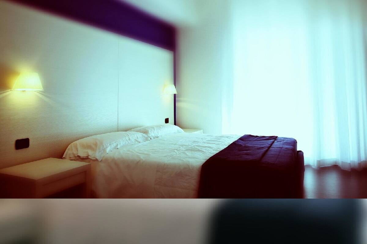 A hotel room with a bed, bedside tables, and wall-mounted lamps.