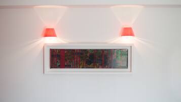 A framed artwork illuminated by two wall-mounted lights on a plain white wall.