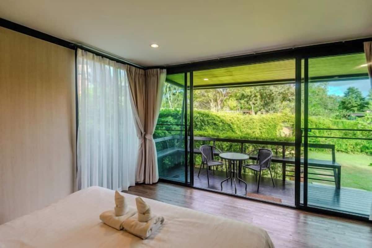 Ein Schlafzimmer mit großem Fenster, einem Bett, einem Sessel und einem Tisch.