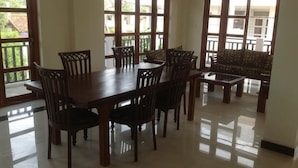 A dining area with a wooden table and chairs, large windows, and a patterned sofa. - Blue Coast View (Negombo)