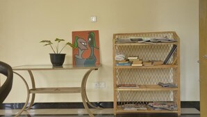 A room with a glass-top table, a potted plant, a colorful painting, and a wooden bookshelf filled with books and magazines. - Blue Coast View (Negombo)