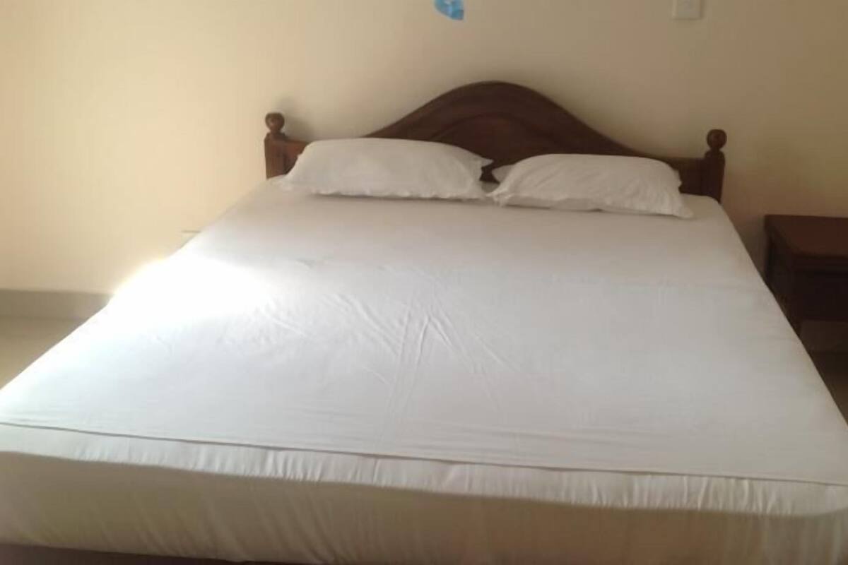 A single bed with a wooden headboard and white bedding in a room with plain walls and a small wooden nightstand.