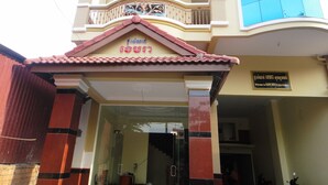 A hotel entrance with a tiled roof, a balcony with decorative railings, and a sign welcoming guests. - Khemra I Guesthouse (Kampot)