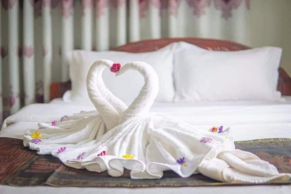 Un lit bien fait, avec du linge de lit blanc et une disposition décorative des serviettes en forme de cygnes sur une tête de lit en bois.