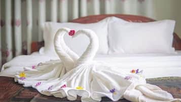 A neatly made bed with white linens and a decorative towel arrangement in the shape of swans on a wooden headboard.