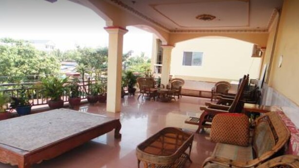 A covered outdoor seating area with a table and chairs, surrounded by potted plants. - Khemra I Guesthouse (Kampot)