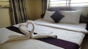 A hotel room with a neatly made bed, a purple throw blanket, and a heart-shaped towel decoration. - Khemra I Guesthouse (Kampot)