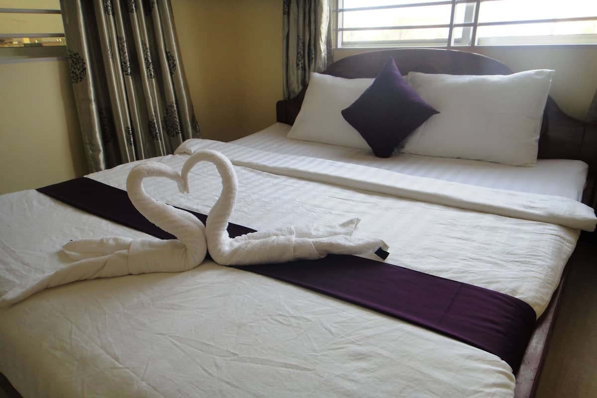 Une chambre d’hôtel avec un lit parfaitement fait, un plaid violet et une serviette décorative en forme de cœur.