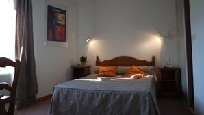 Une chambre à coucher avec un lit, une tête de lit en bois, deux tables de chevet, une petite table avec une plante et une affiche accrochée au mur.