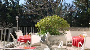 Une terrasse extérieure avec des nappes rouges, des chaises blanches et un vase décoratif servant de centre de table.