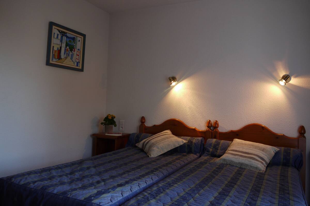 Una cama doble con cabecera de madera, dos mesitas de noche y un tocador con una lámpara. En la pared hay un cuadro enmarcado.