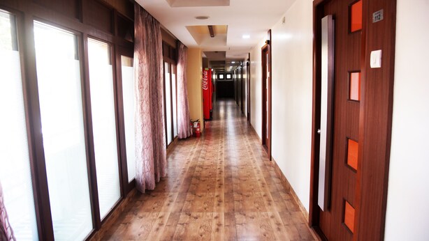 A hotel hallway with wooden flooring, large windows with curtains, and doors with nameplates. - Hotel Indiana Inn (Navi Mumbai)