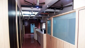 A hallway with wooden paneling, ceiling fans, and a reception desk. - Hotel Indiana Inn (Navi Mumbai)