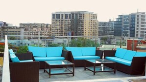 A rooftop terrace with outdoor furniture, including sofas and tables, overlooking a cityscape with buildings. - Hotel Aureole (Mumbai)