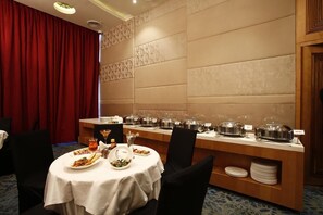 A dining area with a buffet setup, including a long table with food containers and a separate round table with plates and glasses. - Hotel Aureole (Mumbai)