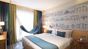 A hotel room with a large bed, a desk with a lamp, a chair, a hanging hammock, and a wall with building drawings. - Hotel Aureole (Mumbai)