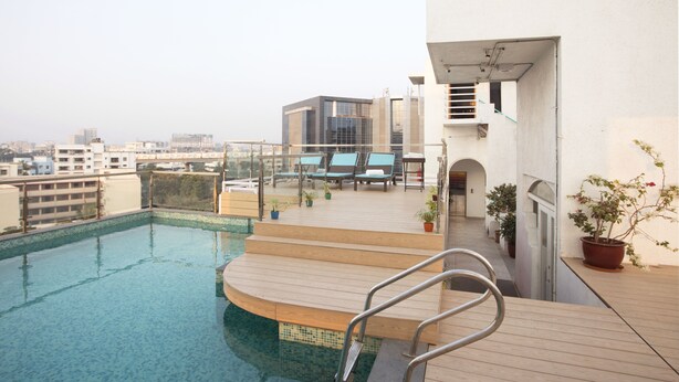 A rooftop pool with a wooden deck, lounge chairs, and potted plants. - Hotel Aureole (Mumbai)