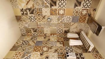 A bathroom with a shower area featuring a variety of patterned tiles. There are two towels on the floor and a towel rack on the wall.
