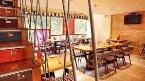 A restaurant with multiple tables and chairs, wooden cabinets, and a TV mounted on the wall. - Hotel Aureole (Mumbai)