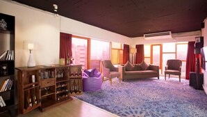 A living room with a sofa, armchairs, a bookshelf, and a large window with curtains. - Hotel Aureole (Mumbai)