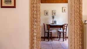 A dining area with a wooden table and chairs, framed pictures on the wall, and a curtain in the doorway. - Agriturismo La Fonte (Bevagna)