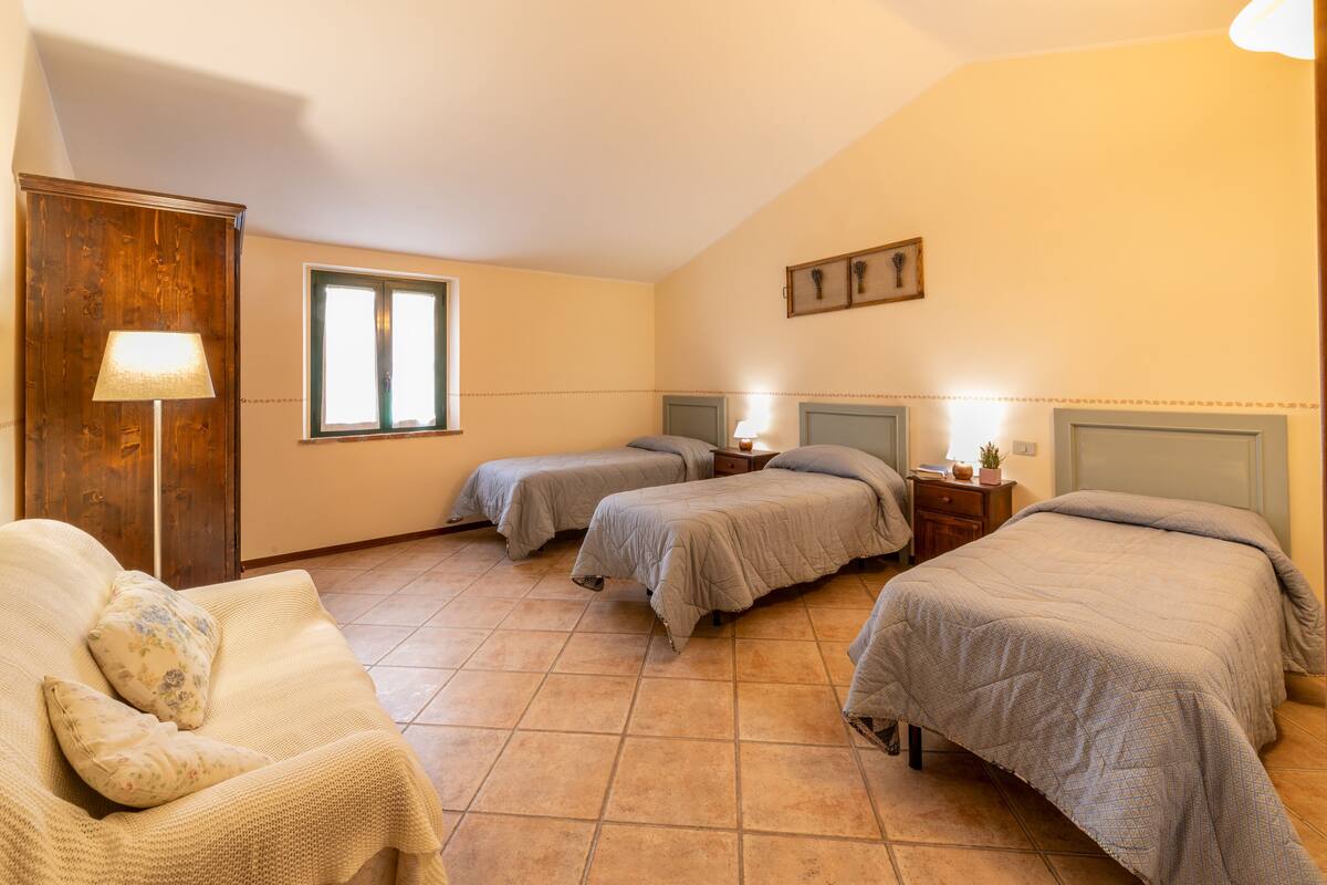 A bedroom with three beds, a sofa, a wooden wardrobe, and a window.