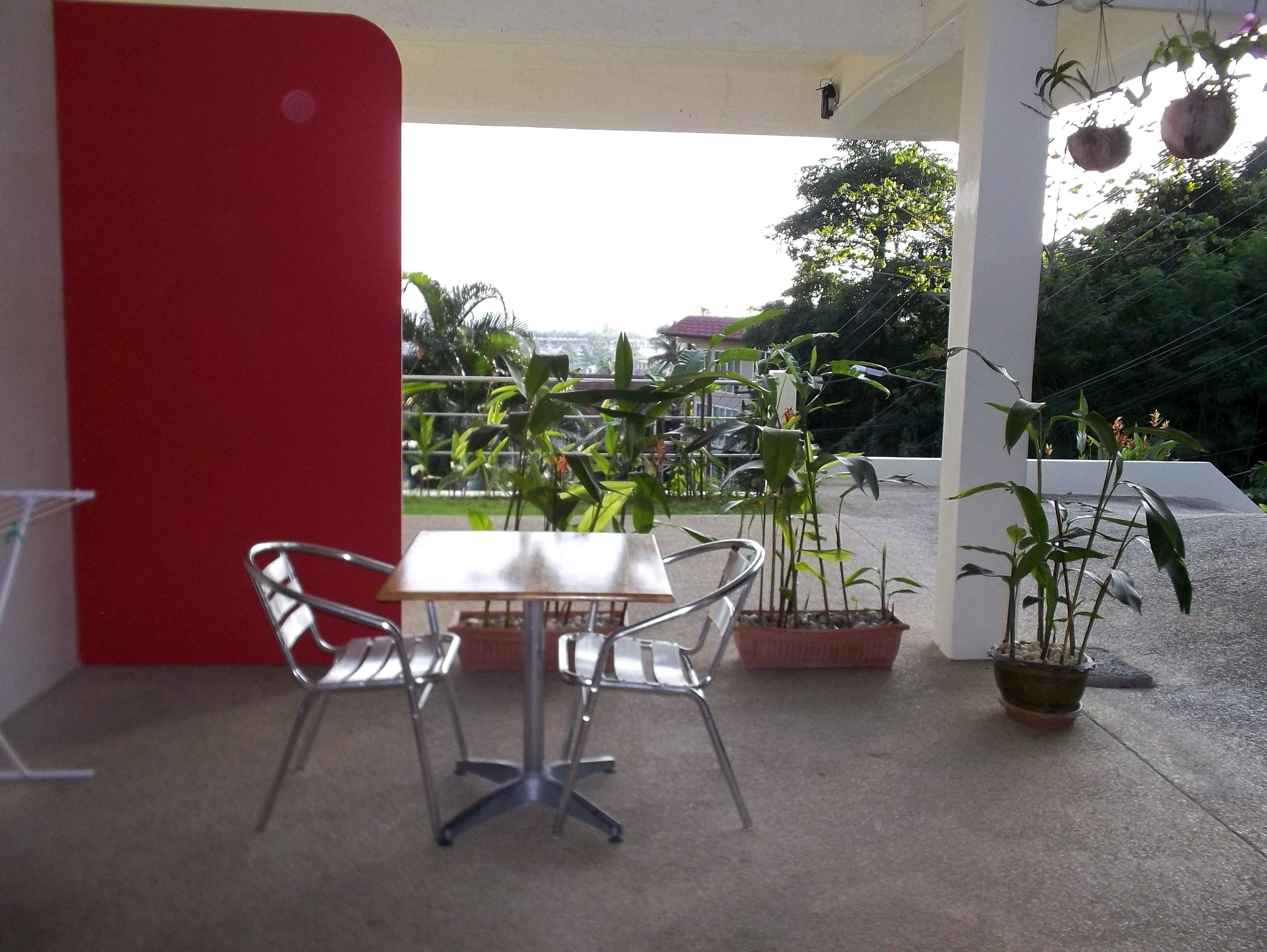 A covered outdoor seating area with a table and chairs, surrounded by potted plants and a view of the cityscape.