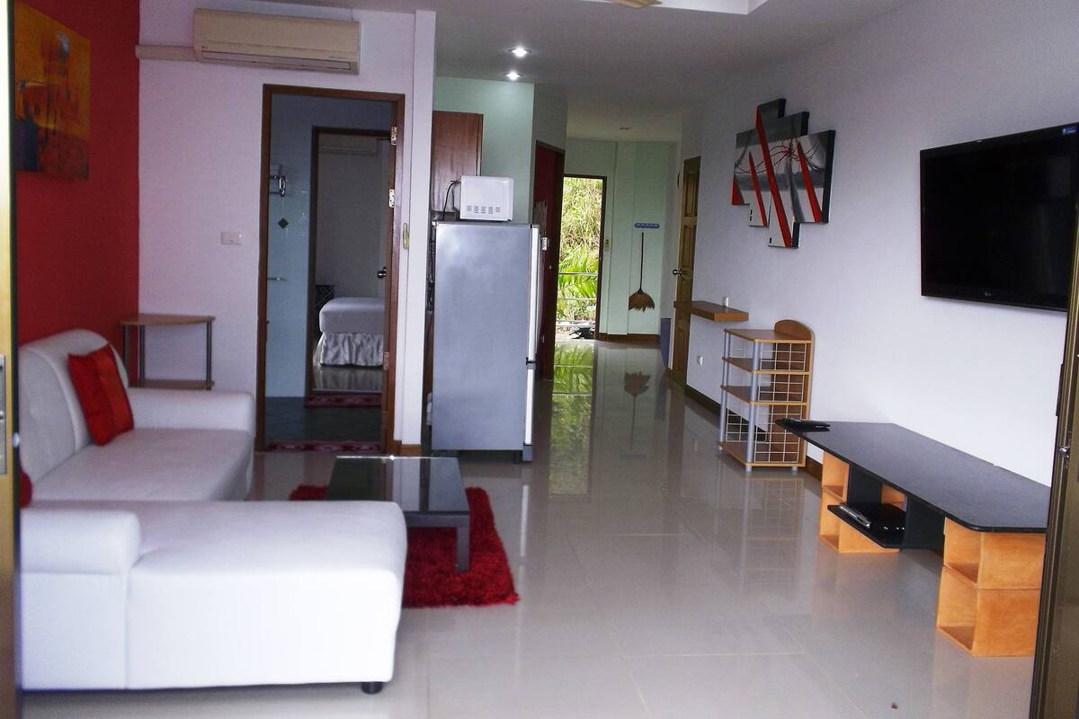 Uma sala de estar moderna com um sofá branco, um tapete vermelho, uma televisão de tela plana e um ventilador de teto.