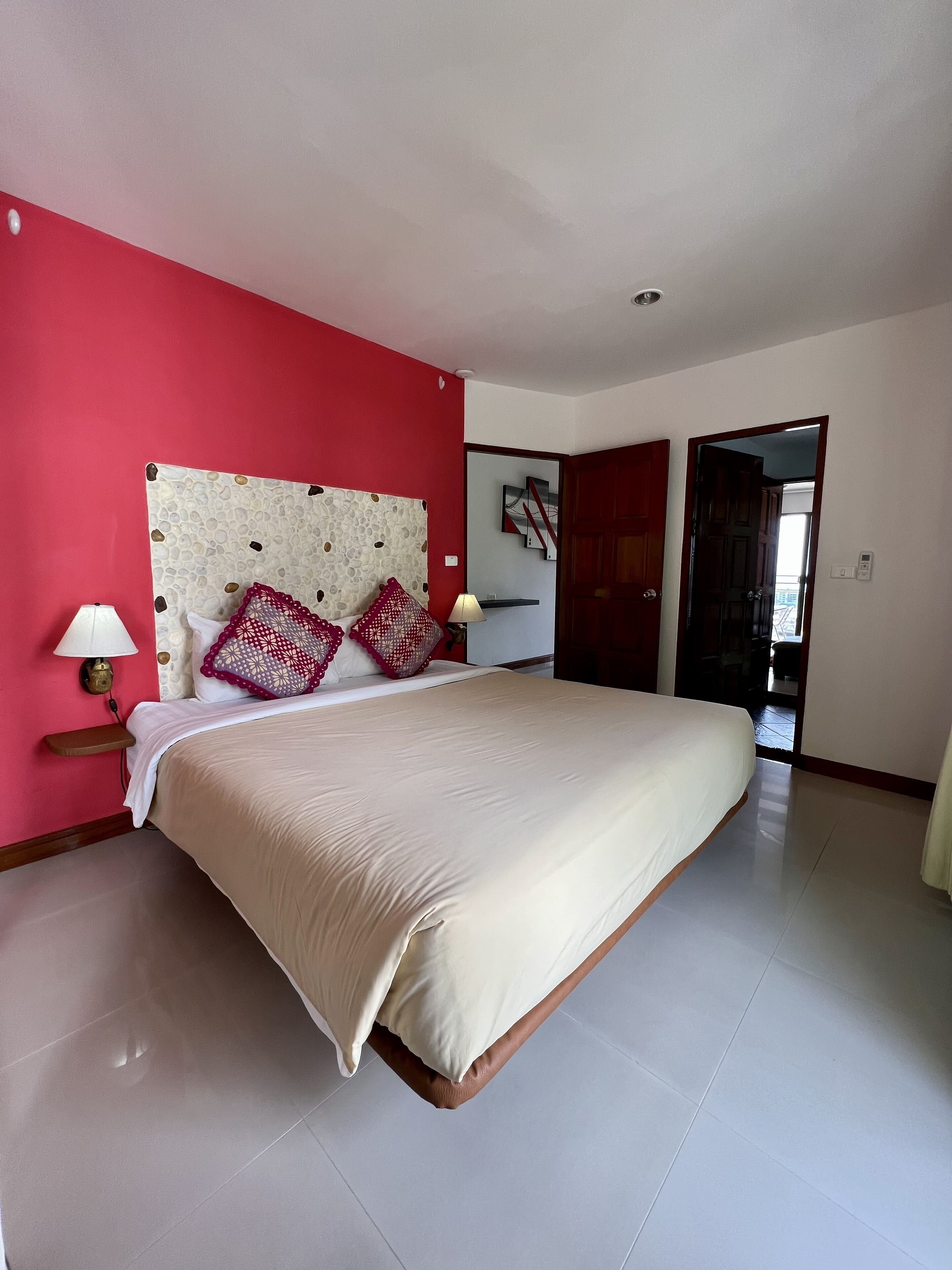 A bedroom with a large bed, a nightstand, a lamp, and a red accent wall.