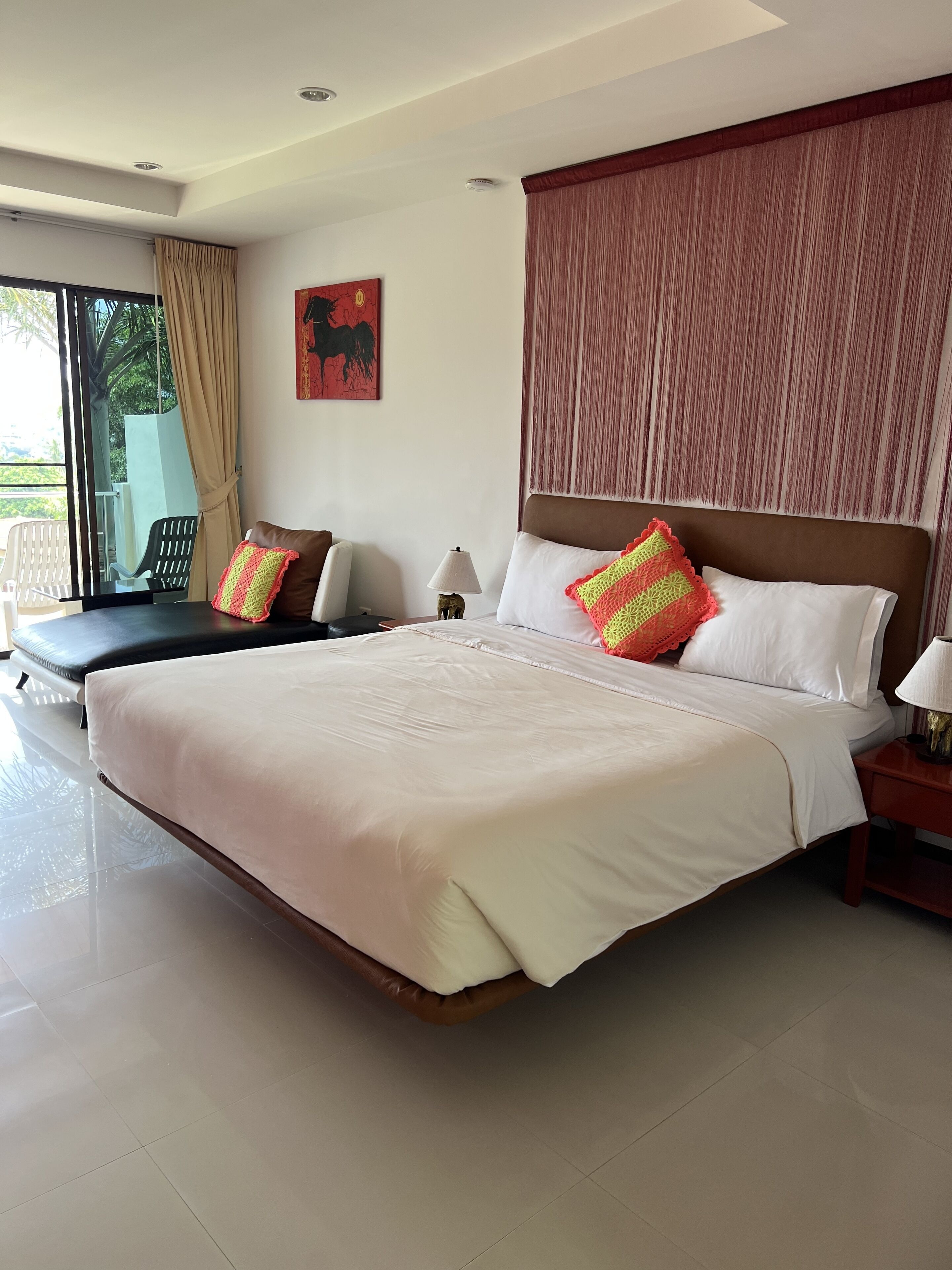 A spacious bedroom with a large bed, a nightstand, a lamp, and a window with curtains.