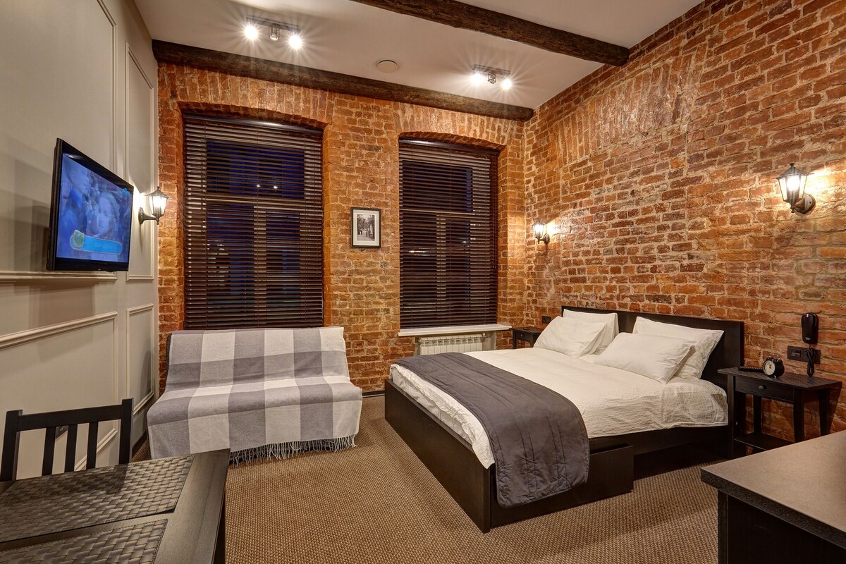 A bedroom with a brick wall, a bed, a desk, and a chair.