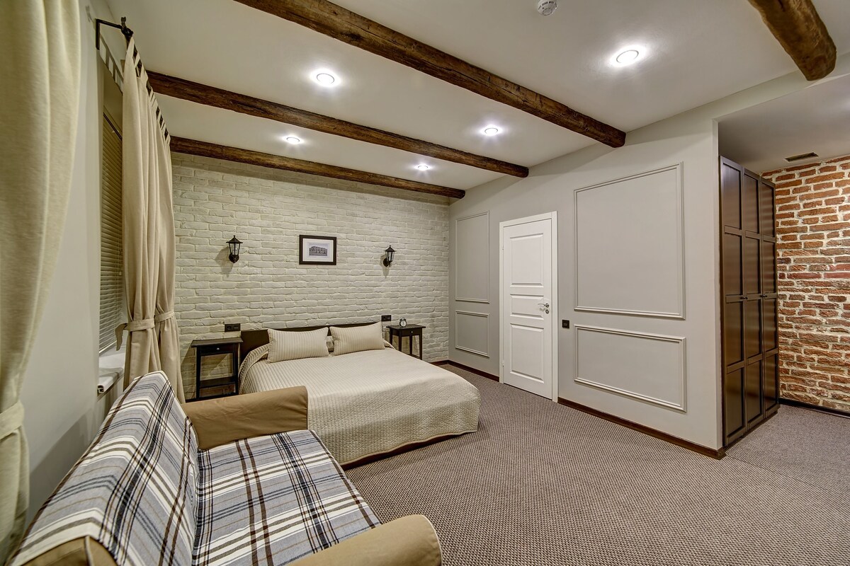 A bedroom with a bed, a sofa, a nightstand, and a brick wall.