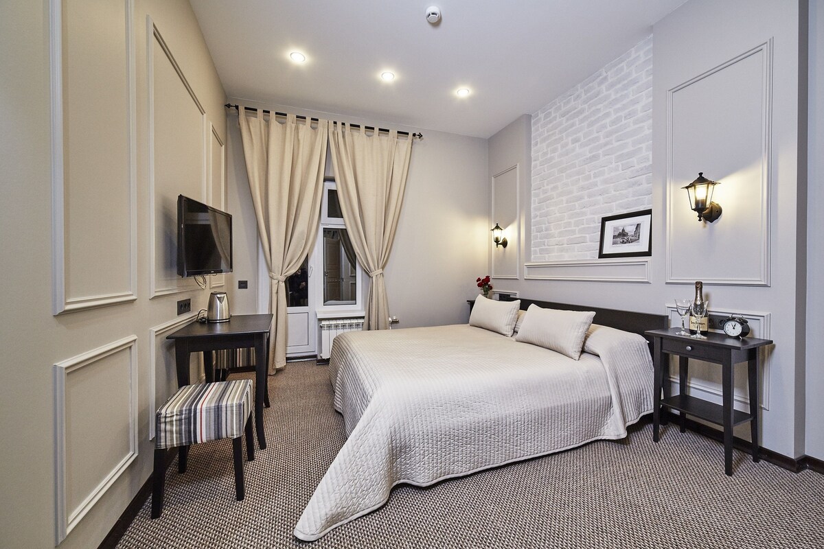 A hotel room with a large bed, a desk with a chair, a television, and a window with curtains.