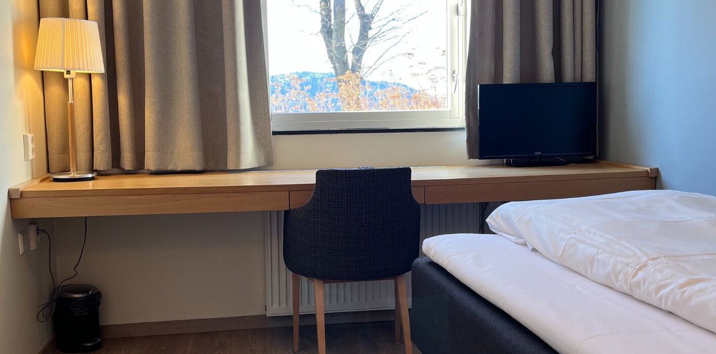 Una habitación de hotel con un escritorio de madera, televisión, una silla y una cama.