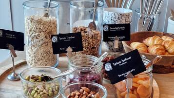 Variedad de alimentos sobre una tabla de madera, como granos, nueces, frutas secas y pasteles, cada uno con su nombre.