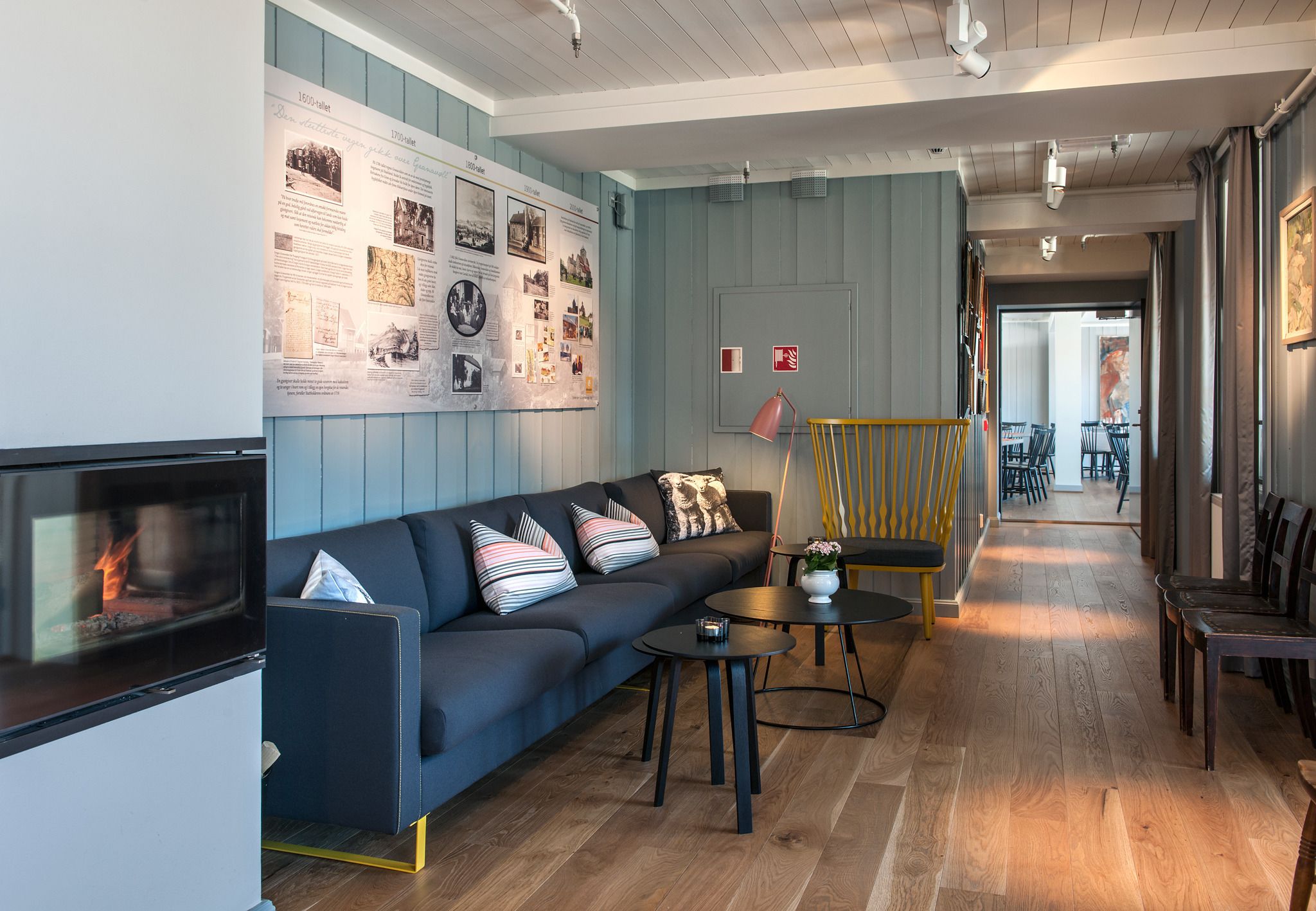 Un salon moderne avec un canapé bleu foncé, une cheminée, un plancher en bois et un mur orné d’affiches informatives.