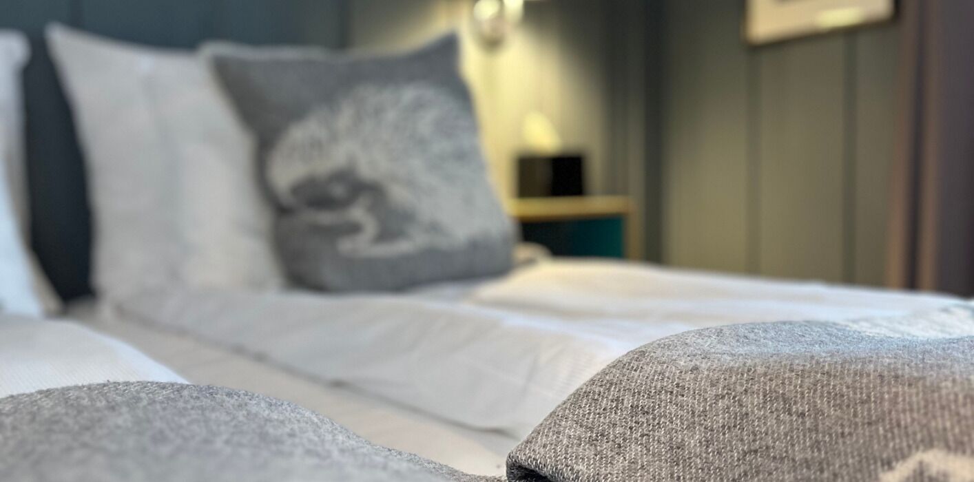 Un letto con lenzuola bianche e un cuscino grigio.