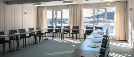 A conference room with a long table, chairs, and large windows with curtains.