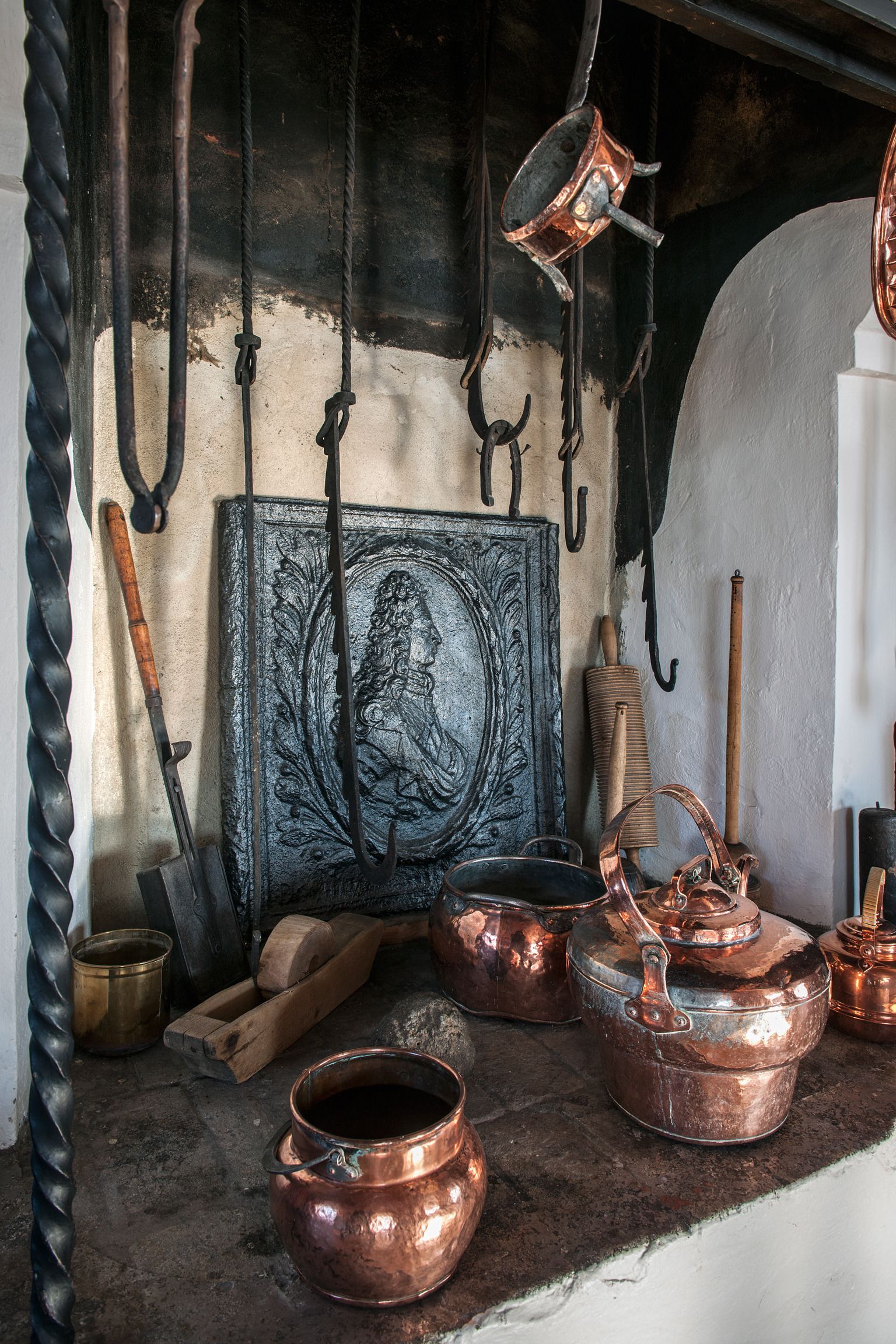 A rustic kitchen with copper cookware, wooden utensils, and a decorative metal plate.